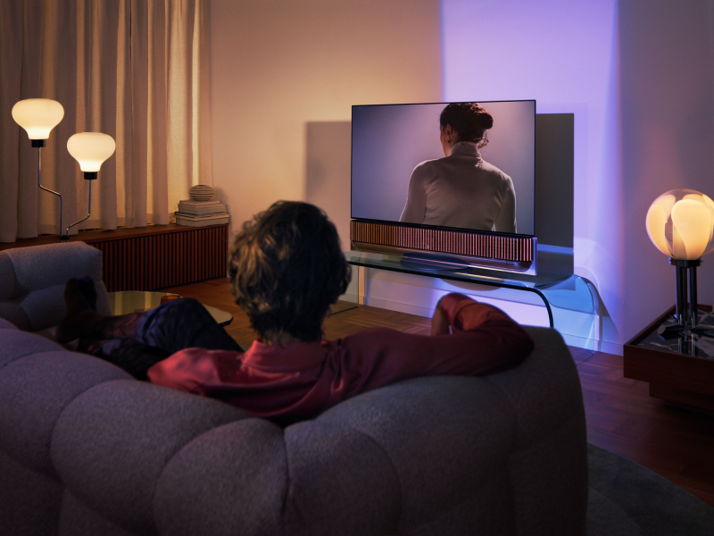A man relaxing in a living room with a TV and Beosound Theatre soundbar